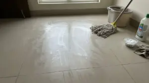 Pavimento con aloni visibili dopo la pulizia, vicino a uno straccio, secchio e detersivo