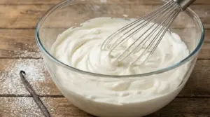 Ciotola di vetro con crema chantilly e frusta da cucina su un tavolo di legno
