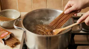Una persona cuoce spaghetti integrali in una pentola d'acqua bollente su un fornello da cucina.