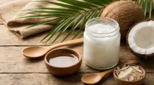 Barattolo di olio di cocco con cocco fresco e cucchiai su tavolo in legno