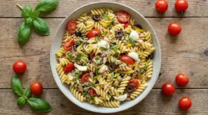 Piatto di pasta fredda con pomodorini, olive, tonno e basilico su tavolo rustico