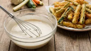 Ciotola con pastella e frusta accanto a verdure fritte croccanti su piatto