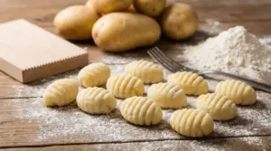 Gnocchi fatti in casa crudi su un tavolo infarinato con patate e farina sullo sfondo