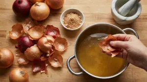 Mano che aggiunge bucce di cipolla in una pentola con brodo, accanto a cipolle e strumenti da cucina