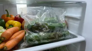 Zucchine marce in un sacchetto di plastica all'interno del frigorifero accanto ad altre verdure.